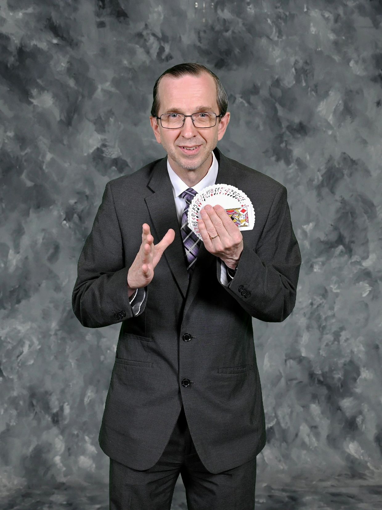 Man in suit performing a card trick with a fan of playing cards.