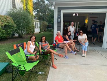Group of women smiling and relaxing in lawn chairs outside a garage during a casual gathering.