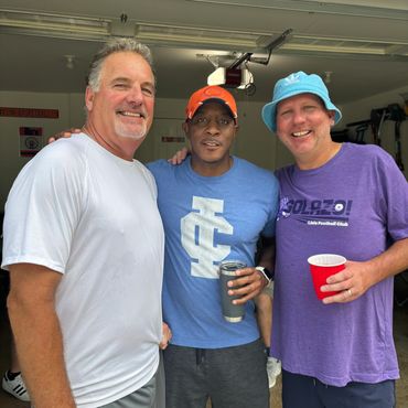 Three men posing happily in a garage, each holding a drink.