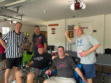 Group of men enjoying a casual gathering in a garage with sports-themed decor.