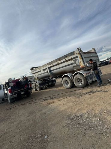 Man working on a trailer attached to a truck in a dusty lot.