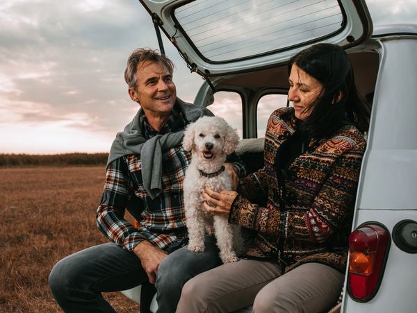 Couple sitting in trunk of their van with the trunk door open and a poodle.