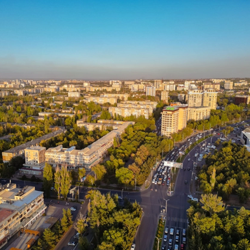 Aerial view of a city with buildings and a busy road surrounded by greenery.