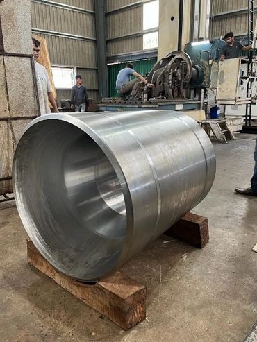 Large cylindrical metal component in an industrial workshop with workers around.