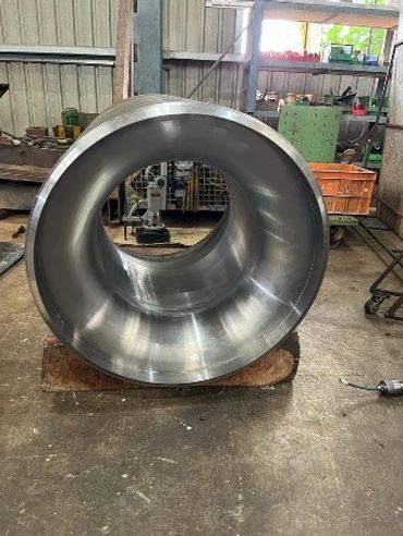 Large polished metal pipe in an industrial workshop setting.