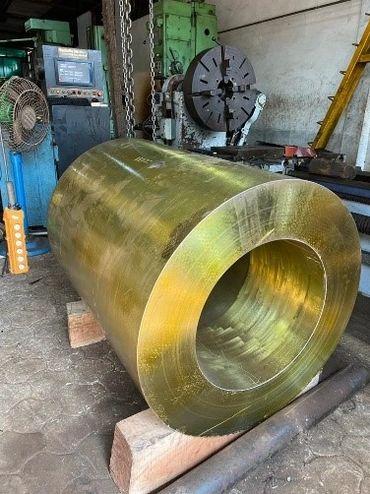 Large cylindrical metal piece in a workshop with machinery in the background.