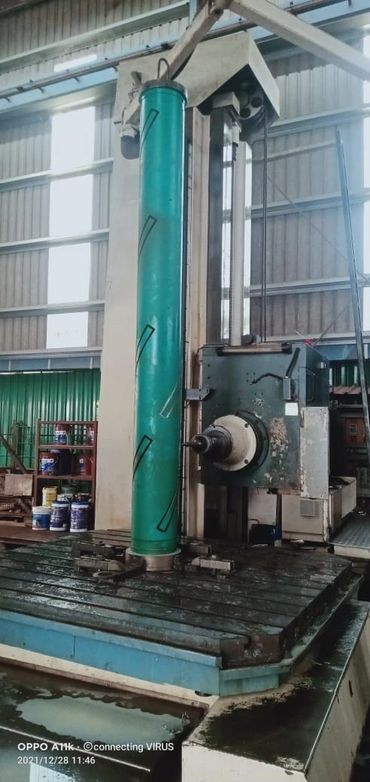 Large vertical industrial machine with green cylindrical part in workshop.