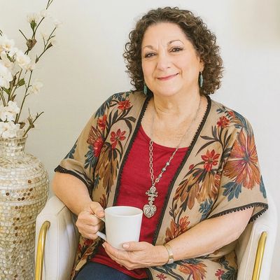 Smiling woman in floral kimono holding a white mug, seated in a stylish chair. holistic life coach