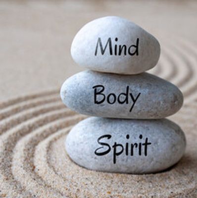 Stacked stones labeled Mind, Body, Spirit on sand with concentric circles.