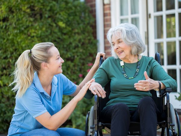 Smiling caregiver attending to a senior woman in wheelchair.