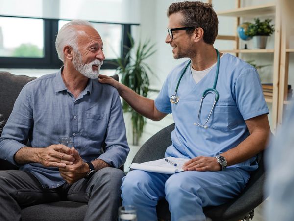 Smiling male nurse in scrubs talking to a senior man.