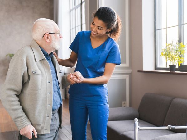 Smiling caregiver assisting a senior man with a walker.