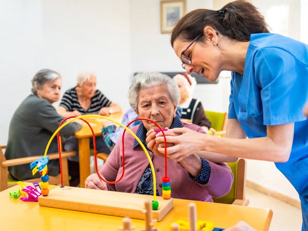 Caregiver assisting senior with occupational therapy activity.