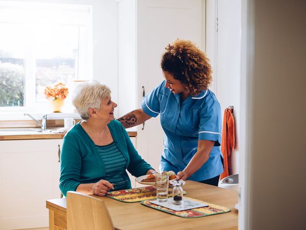 Caregiver serving a meal to a senior woman.