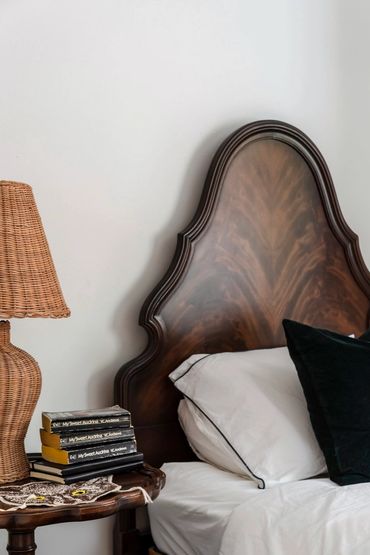 Elegant wooden bed with white linens and a wicker lamp on a side table.
