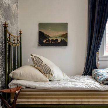 Cozy vintage bedroom with striped bed, antique headboard, and landscape painting.