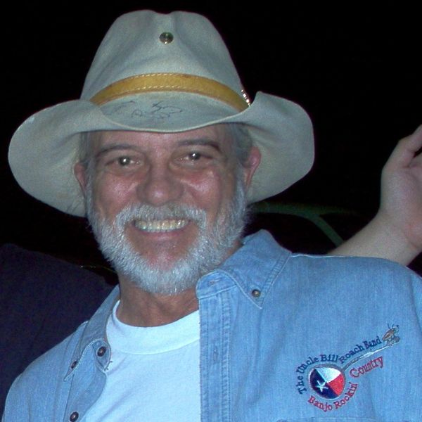 Smiling man wearing a cowboy hat and a denim shirt with a music band logo.