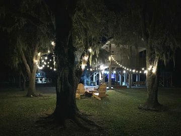 Outdoor string lights illuminate a cozy backyard with wooden chairs at night.