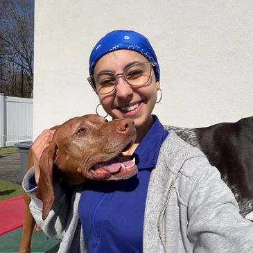 Smiling woman in blue bandana hugs a happy brown dog outdoors.