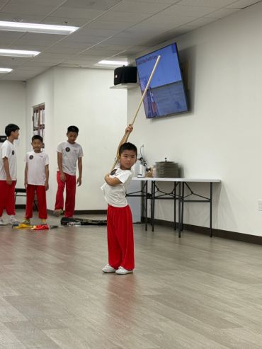 Young boy practicing martial arts with a staff indoors.
