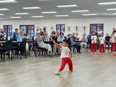 A young boy practices martial arts with an elderly audience watching.
