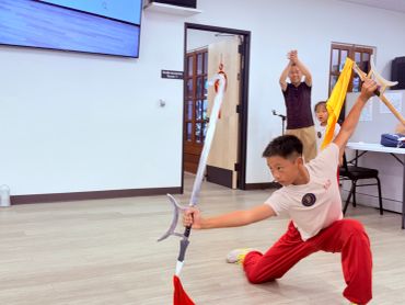 A boy practices martial arts with a weapon indoors.