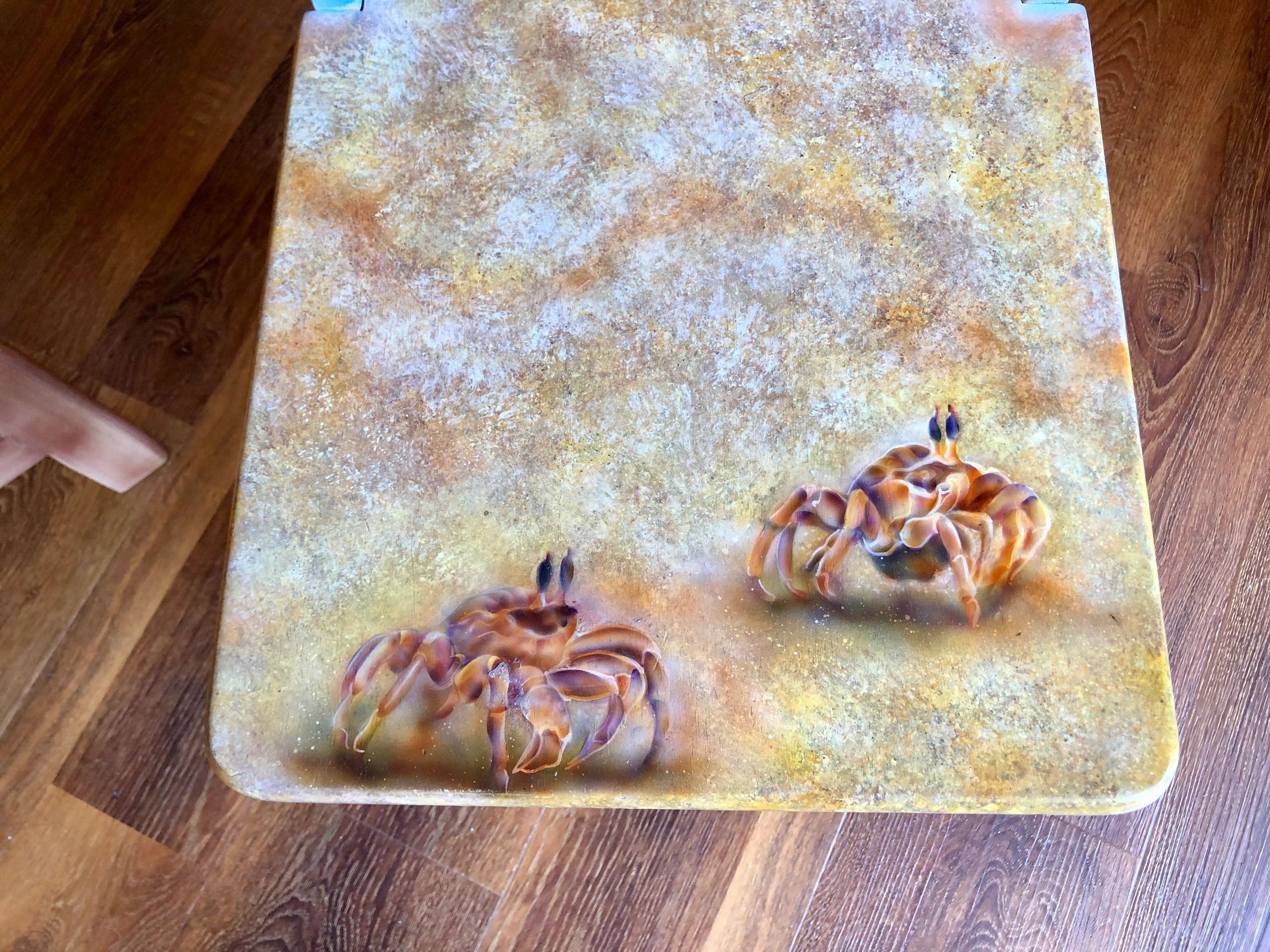 A textured surface with two detailed crab illustrations on a wooden floor.