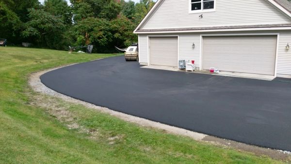 Newly paved black asphalt driveway beside a house garage.