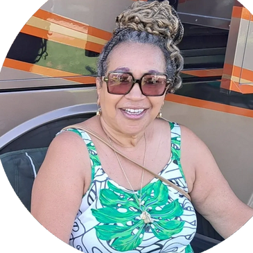 Smiling woman with braided hair wearing sunglasses and a tropical print dress.