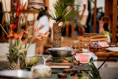 Tropical fruits and flowers arranged on a table with a pineapple centerpiece.