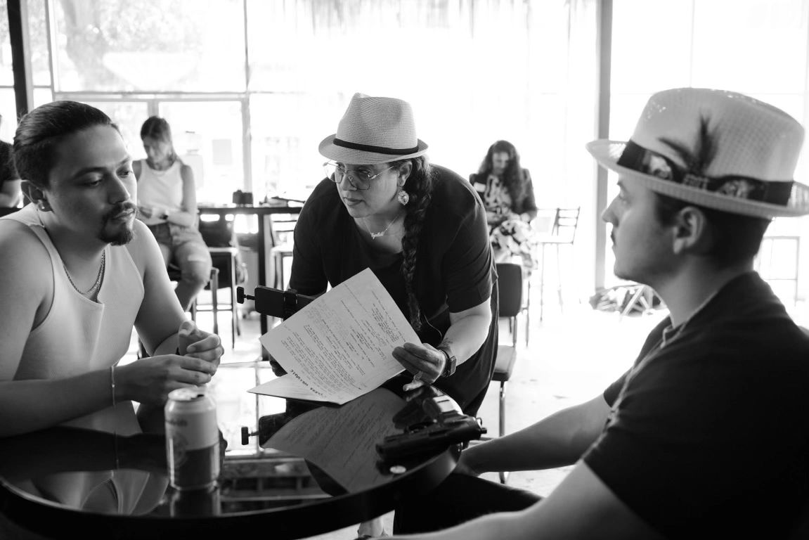 Three people engaged in a serious discussion at a table with documents and a gun.