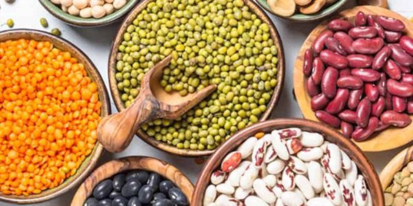 Various colorful legumes displayed in wooden bowls on a white surface.