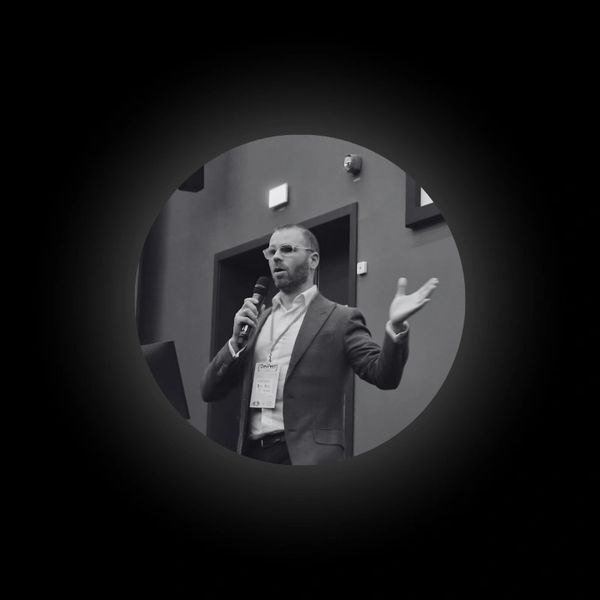 Man in suit speaking into a microphone at a conference.