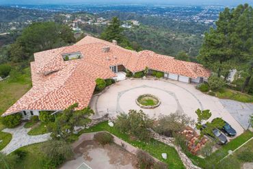 A large hillside mansion with a circular driveway and terracotta roof tiles.