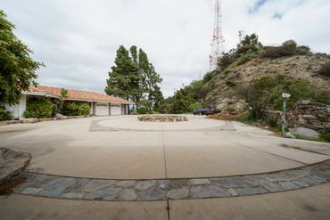 Spacious circular driveway with a stone centerpiece near a hillside house.