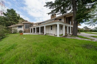 A large house with white pillars and stone accents surrounded by greenery.