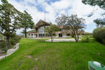 Large house with tall glass windows surrounded by green lawn and trees.