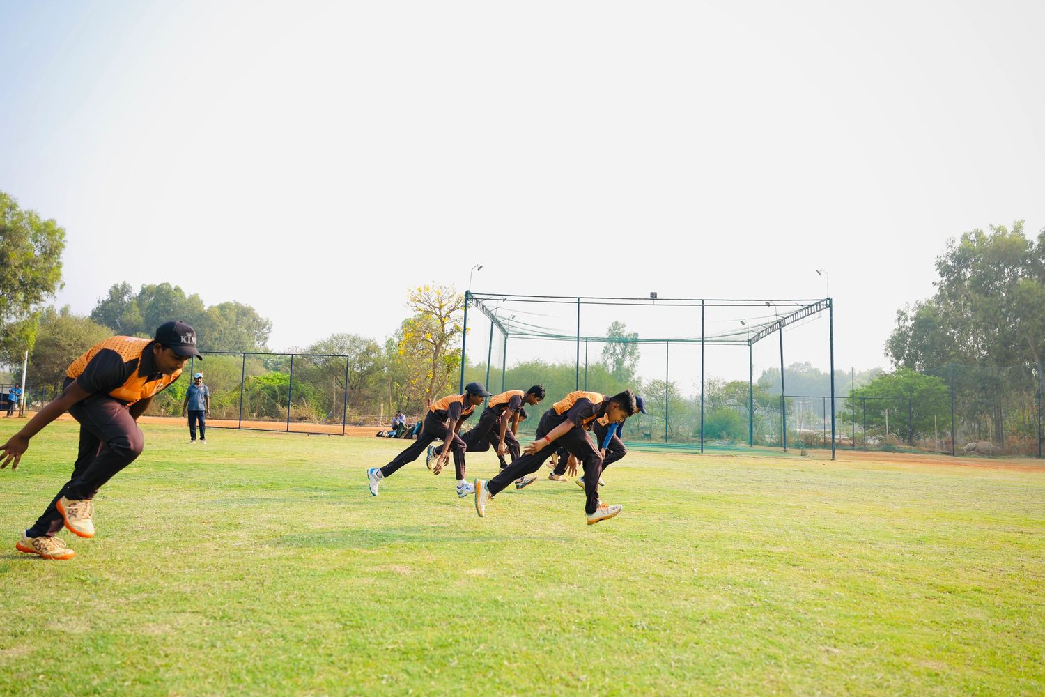 Young cricket players sprinting on a grassy field during practice.