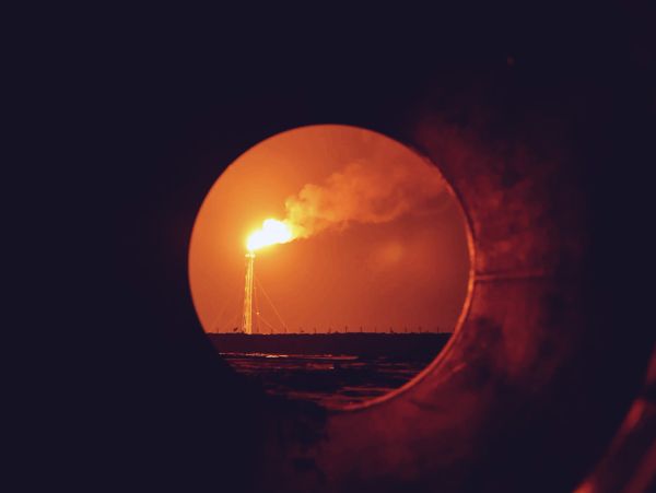 Flaming industrial tower seen through a circular opening at night.