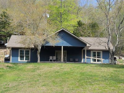 Blue house with front porch surrounded by trees.