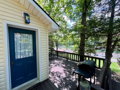 Blue door on yellow house, patio wrapping around right and water of marina in distance through trees