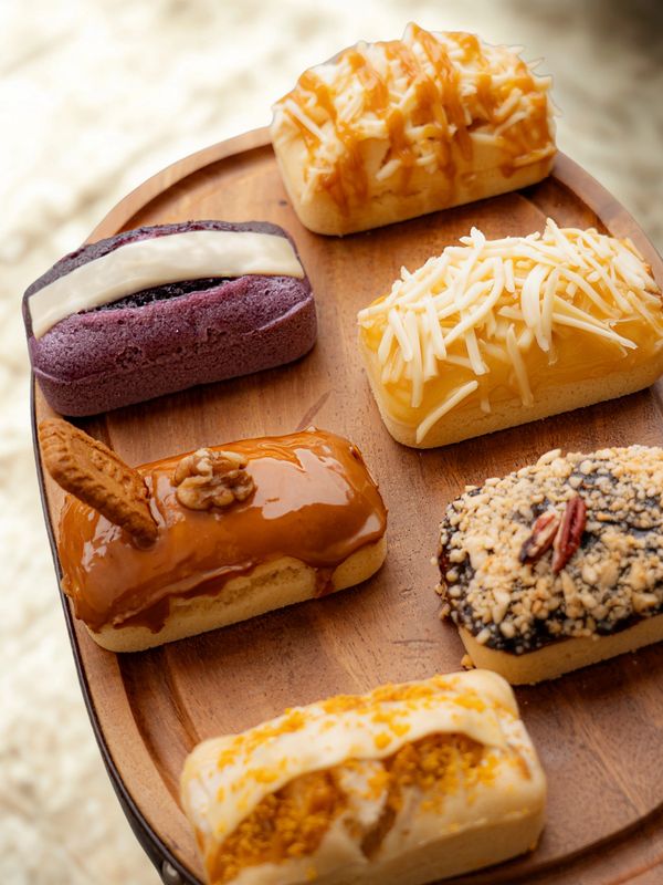 A wooden tray with six assorted mini cakes topped with nuts, cheese, and caramel.