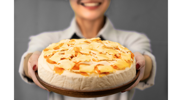 Person holding a cheesecake topped with mango slices and flakes.