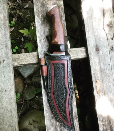 Knife with leather sheath on wooden surface.