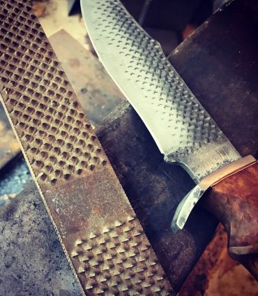 Close-up of a knife blade with patterned texture beside a file tool.