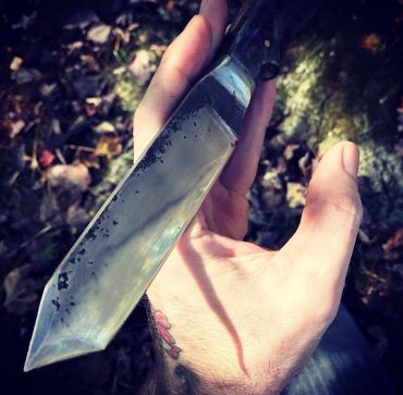 Hand holding a large, sharp knife outdoors.