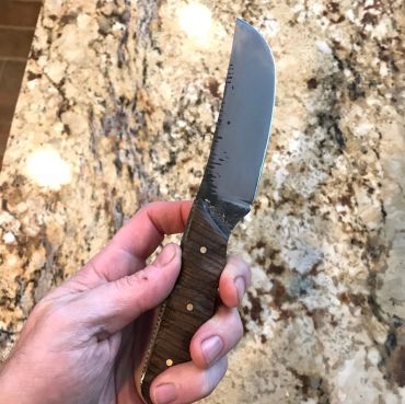 Hand holds a knife with a wooden handle.