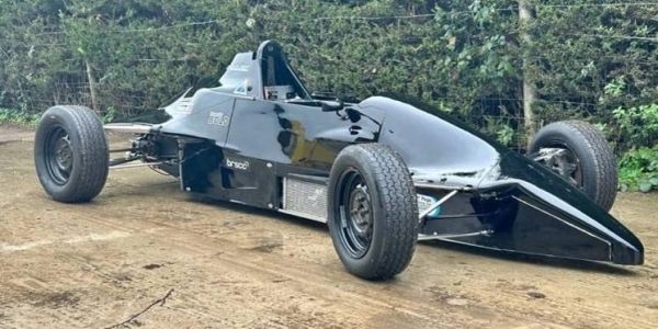 Black single-seater race car on dirt ground.