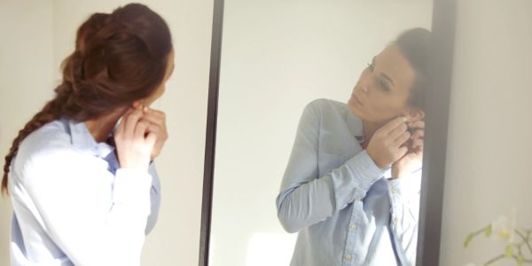Woman putting on earrings in front of a mirror.