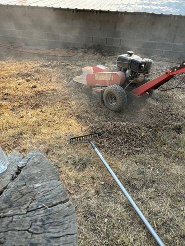 A stump grinder clearing a tree stump in a dry yard with a garden rake nearby.